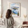 Framed Crater Lake Watercolor Wall Art - In Living Room with Woman Looking at it - Portrait