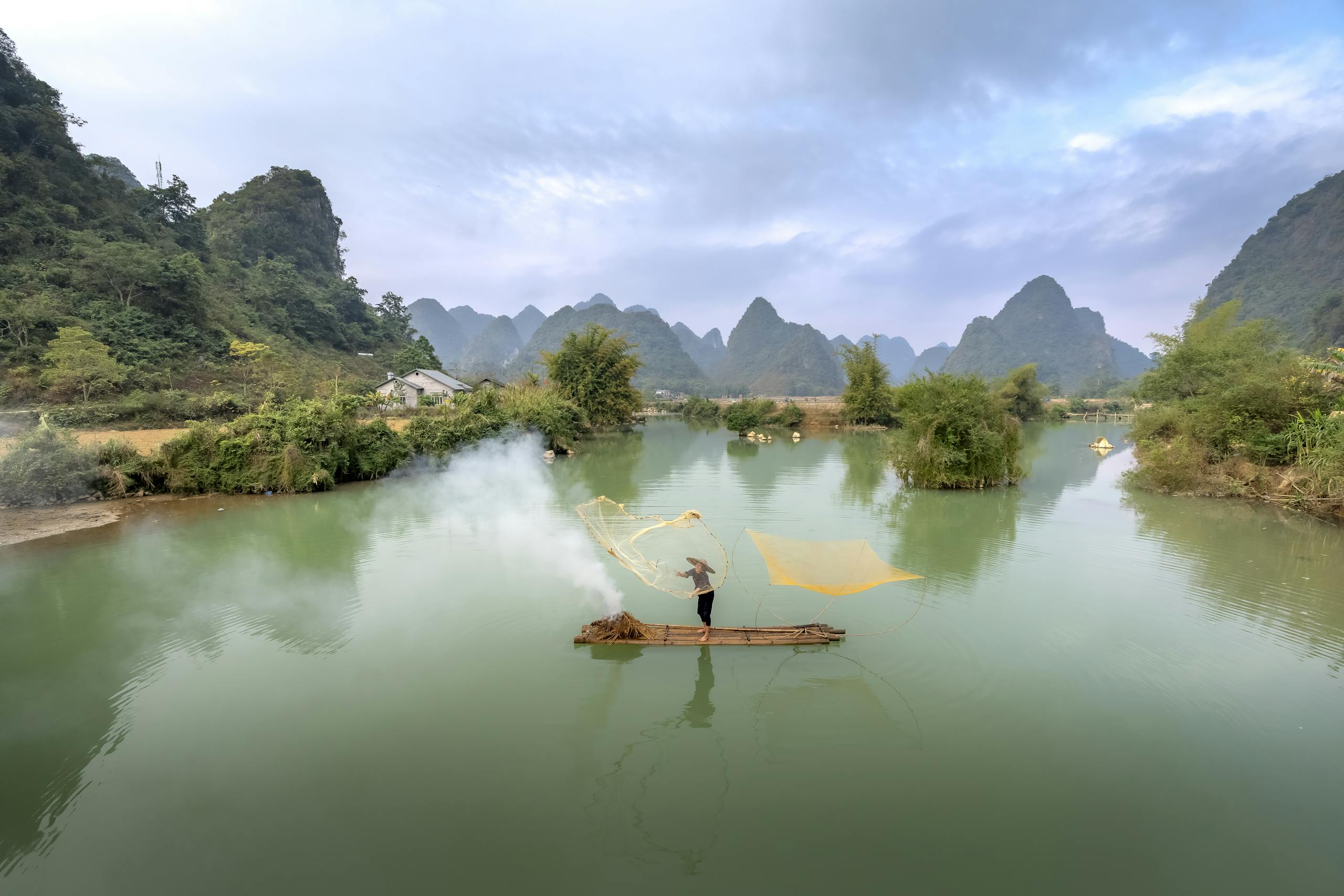 Comprehensive 2-Week Vietnam Travel Itinerary for 2025: North to South Highlights and Planning Tips 3 A fisherman casts a net on a serene river surrounded by lush mountains at dawn, creating a peaceful scene.