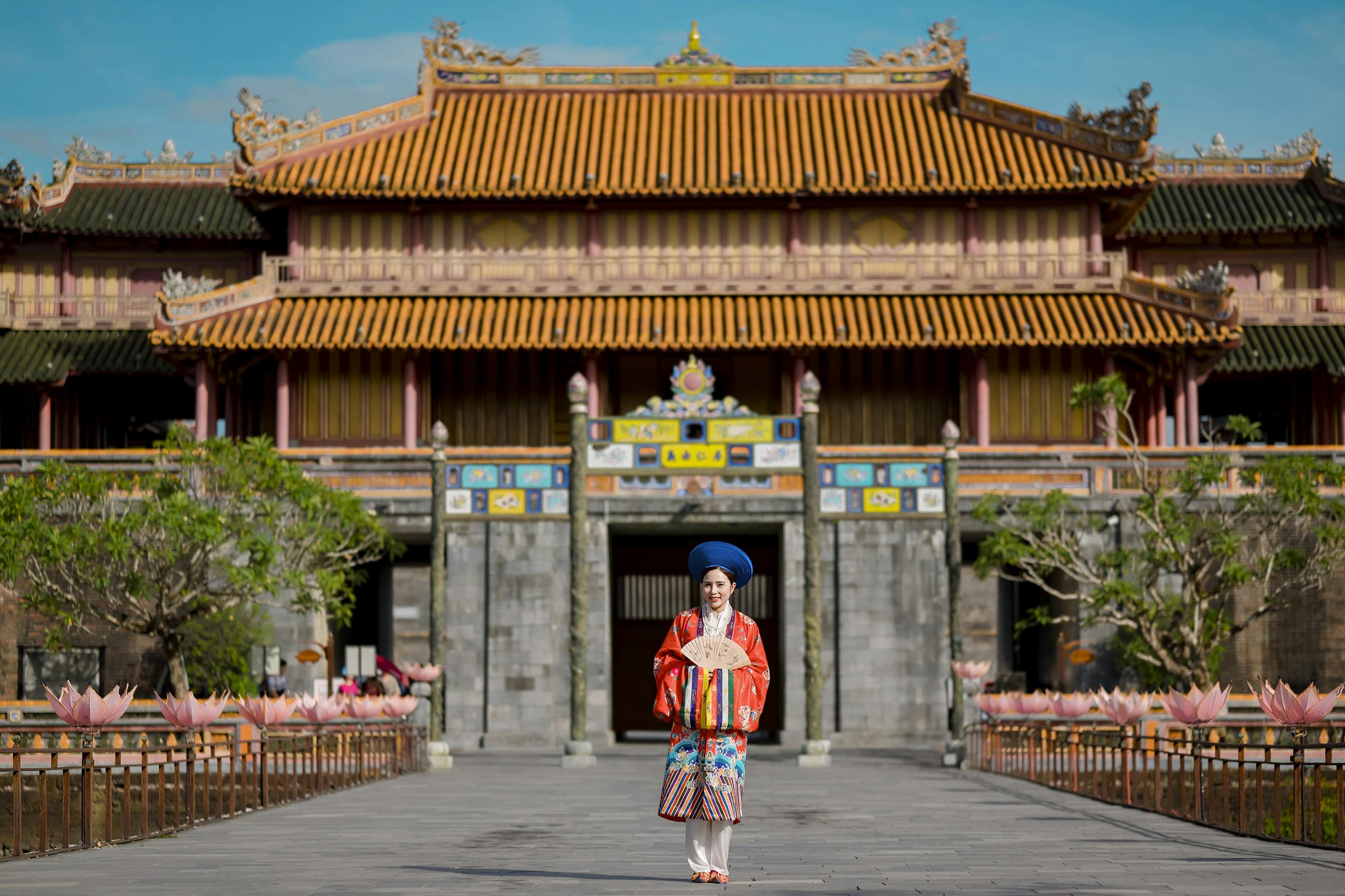 Asian woman in traditional attire stands before Hue Imperial City, Vietnam's historic landmark.