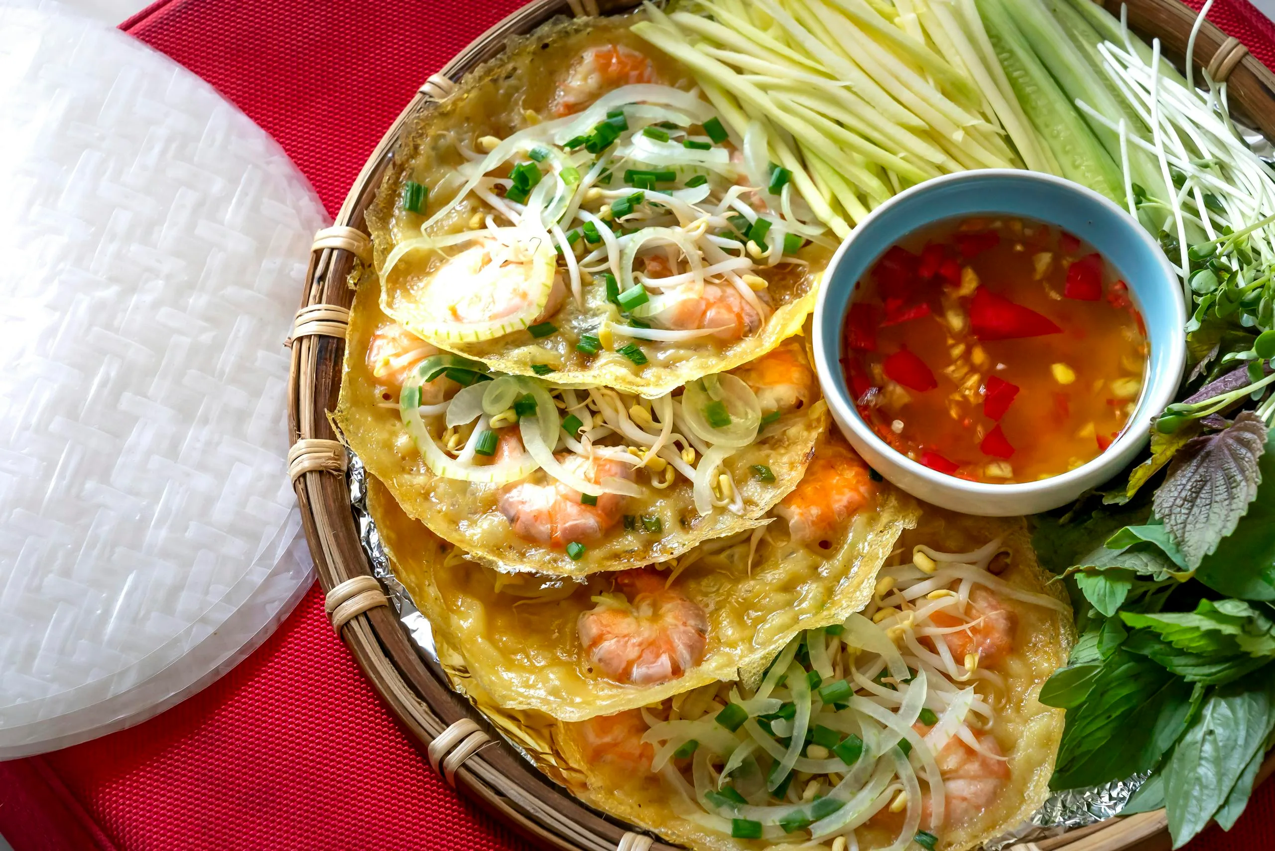 Close-up of traditional Vietnamese crispy pancake served with fresh vegetables and a spicy dip.