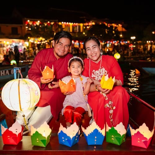 Family in ao dai enjoying lantern festival on a boat at night in Hội An.