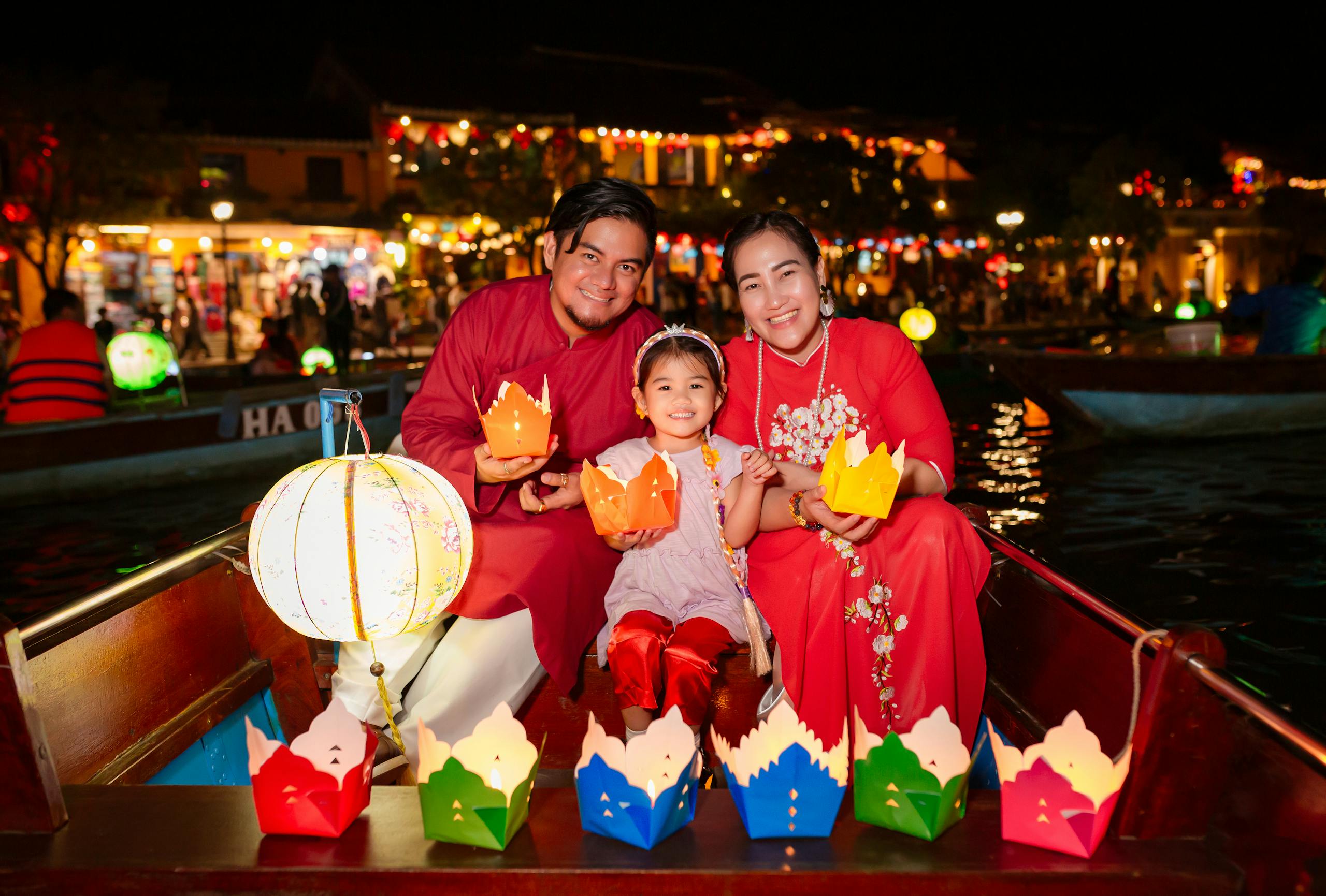 Family in ao dai enjoying lantern festival on a boat at night in Hội An.