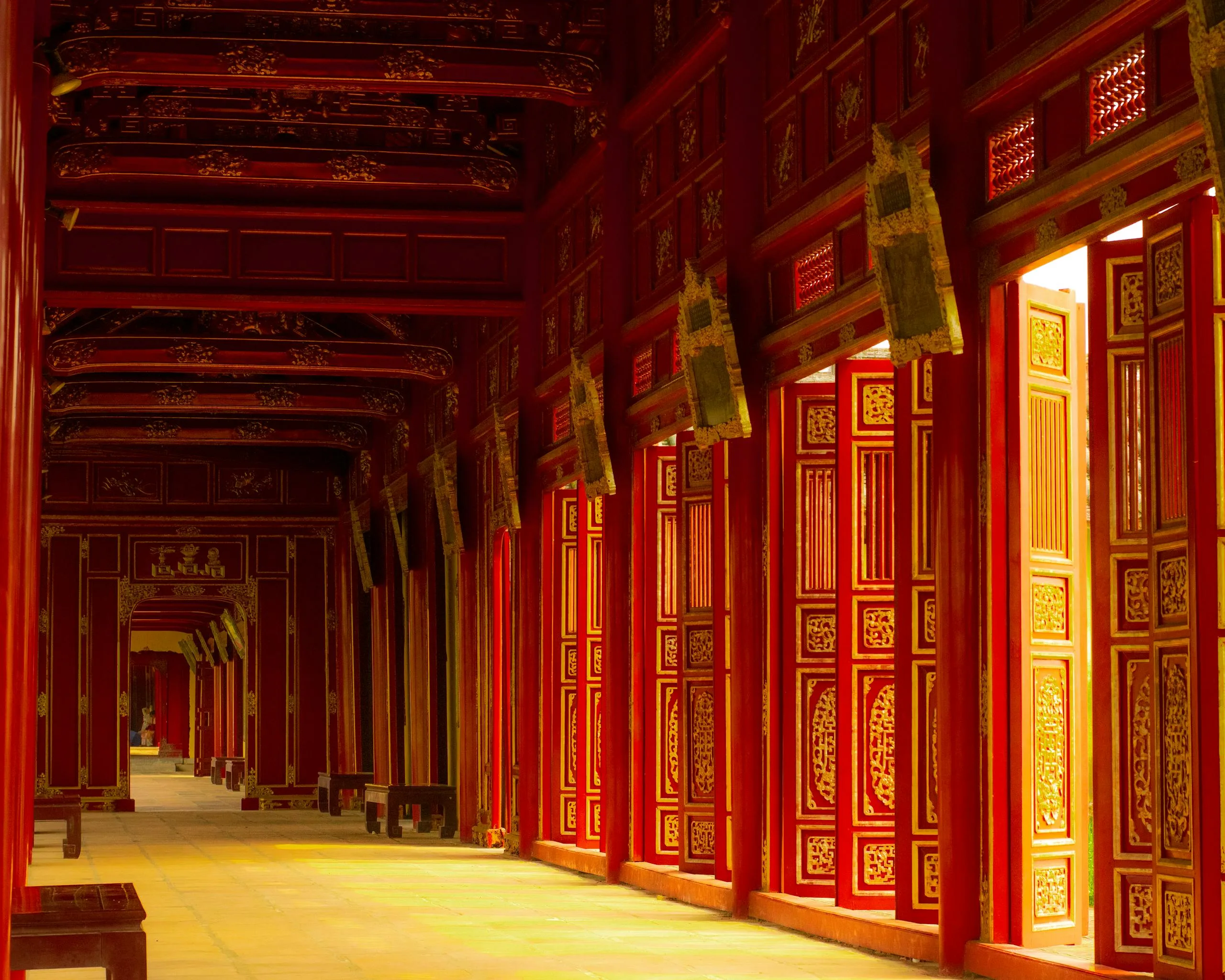 Immersive Cultural Experiences and Royal Cuisine in Hue: A Traveler’s Guide 2025 16 Intricate red corridor with open ornate wooden doors, featuring traditional architecture in warm sunlight.