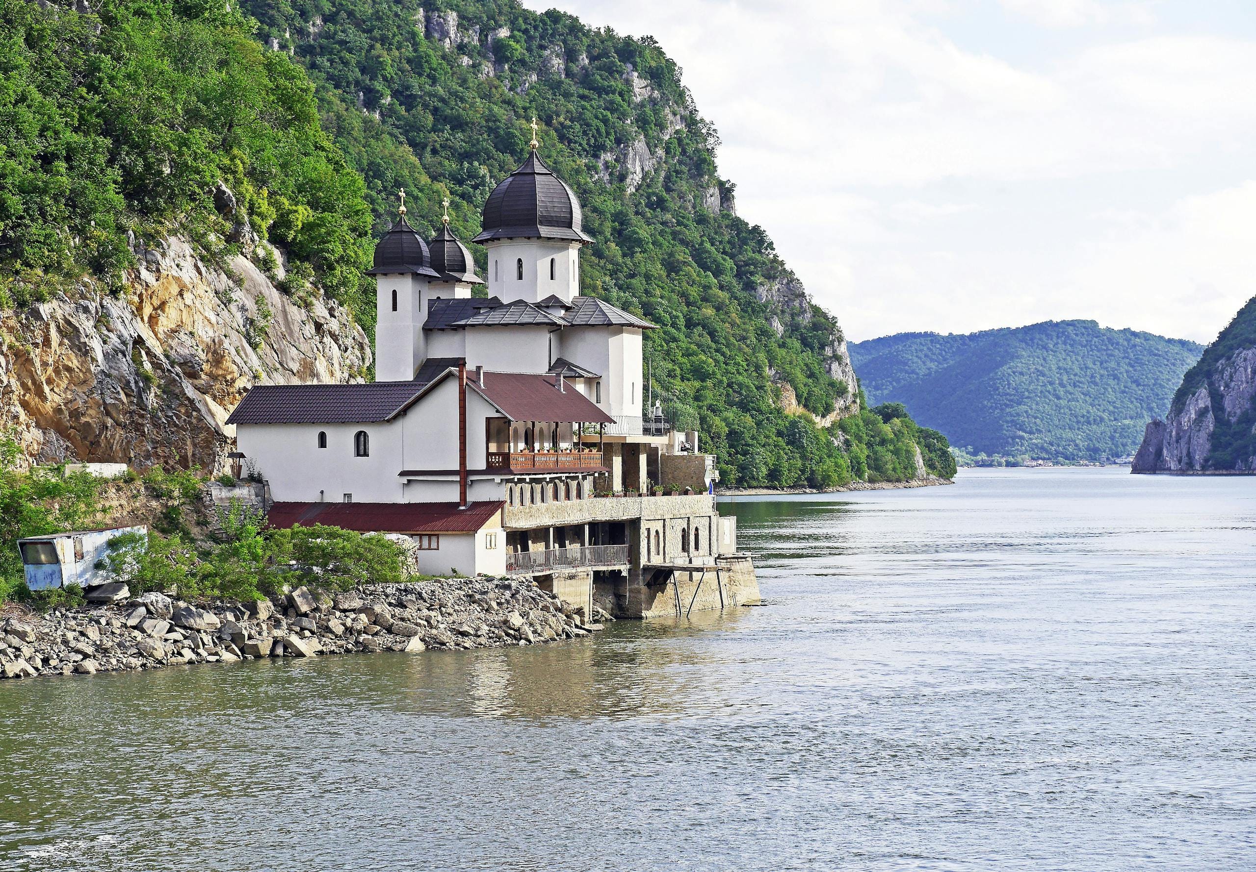Best Cheap Places to Go on Vacation in 2025 — Budget Destinations, Sample Budgets & Money-Saving Hacks 26 Scenic Orthodox monastery by the Danube River gorge in summer, set against lush green mountains.