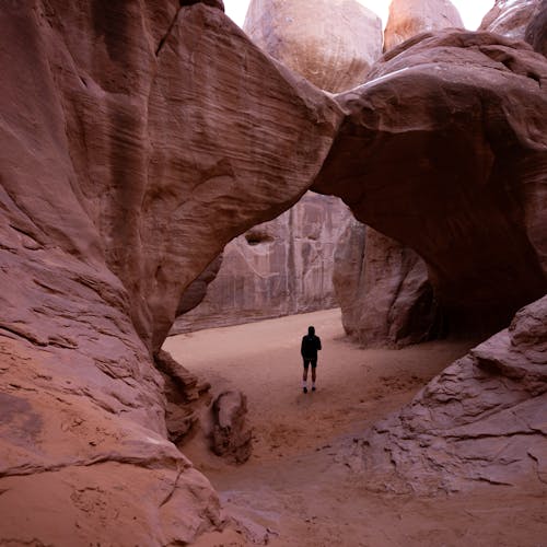 A hiker stands beneath prominent rock formations in Arches National Park, Moab, Utah.