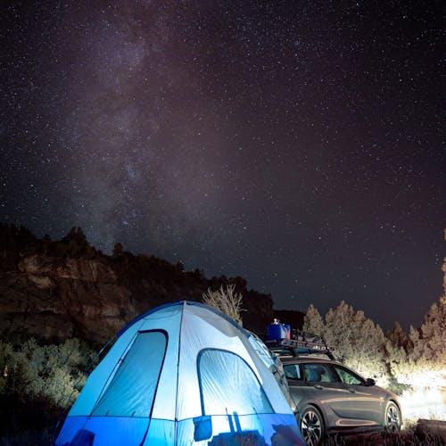 Starry night at a campground with a tent and car in Springdale, Utah.