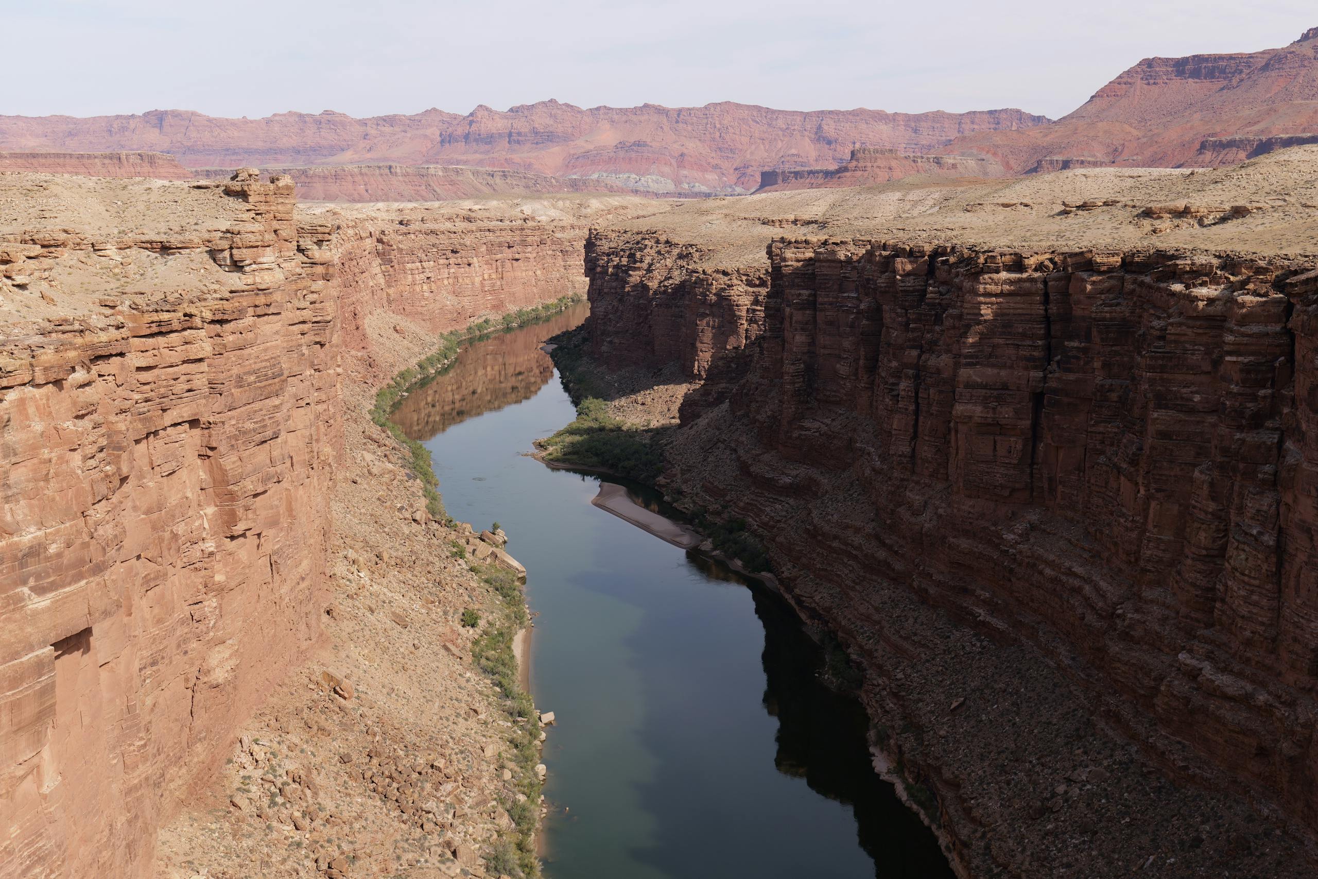 Stunning view of Colorado River carving through the Grand Canyon's red sandstone cliffs under a clear sky.