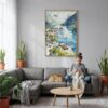 02 - The Fjords Watercolor Canvas Print with Natural Floater Frame - Woman Knitting on grey couch - Vertical.jpg