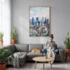 03 - Montreal Skyline Watercolor Canvas Print with Natural Floater Frame - Woman Knitting on grey couch - Vertical.jpg