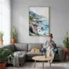05 - Big Sur California Watercolor Canvas Print with Natural Floater Frame - Woman Knitting on grey couch - Vertical.jpg
