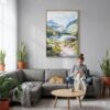 05 - Glacier National Park Watercolor Canvas Print with Natural Floater Frame - Woman Knitting on grey couch - Vertical.jpg