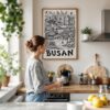 03 - Framed Busan City Art - Pencil Style Art Print hanging in Kitchen with woman making coffee - Vertical.jpg